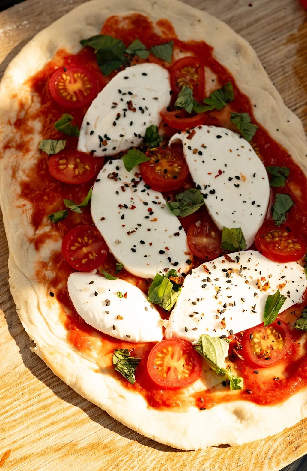 A pizza topped with cherry tomatoes, mozzarella cheese, fresh basil leaves, and sprinkled with black and red pepper flakes.