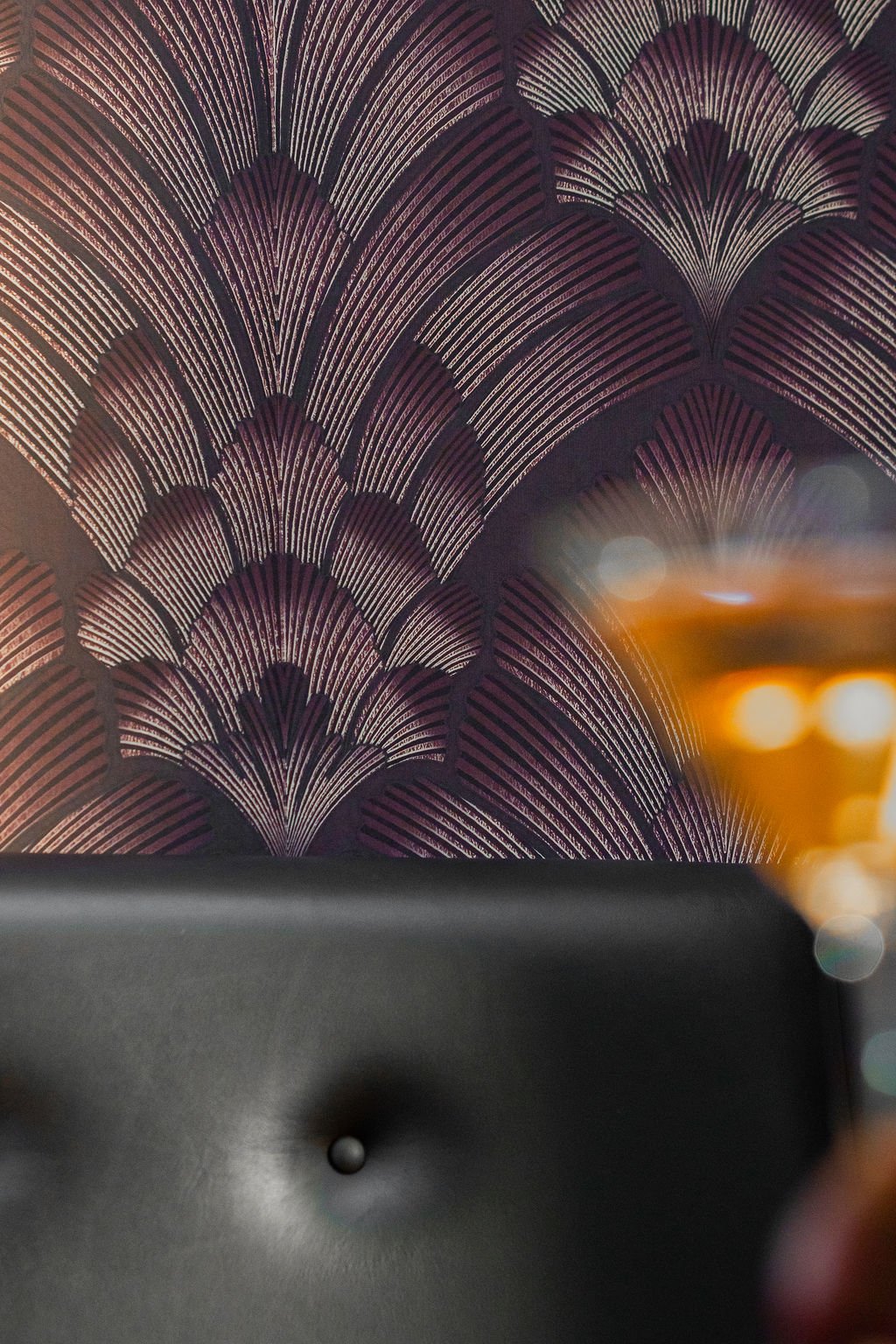 Close-up of a decorative wall with purple and black fan-shaped patterns, with part of a glass of drink and a black surface in the foreground.