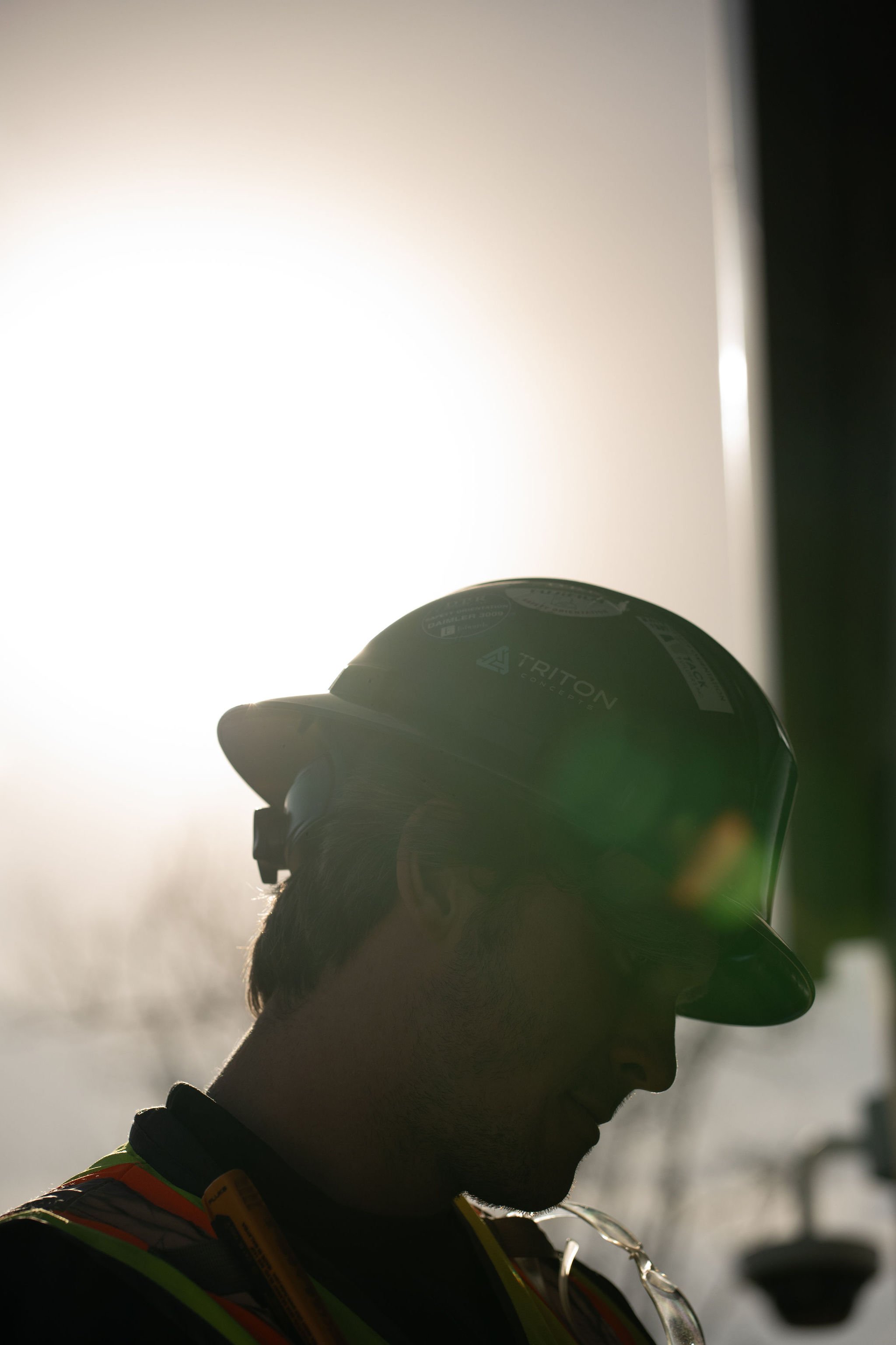 Silhouette of a person wearing a helmet, looking downward, with sunlight in the background.