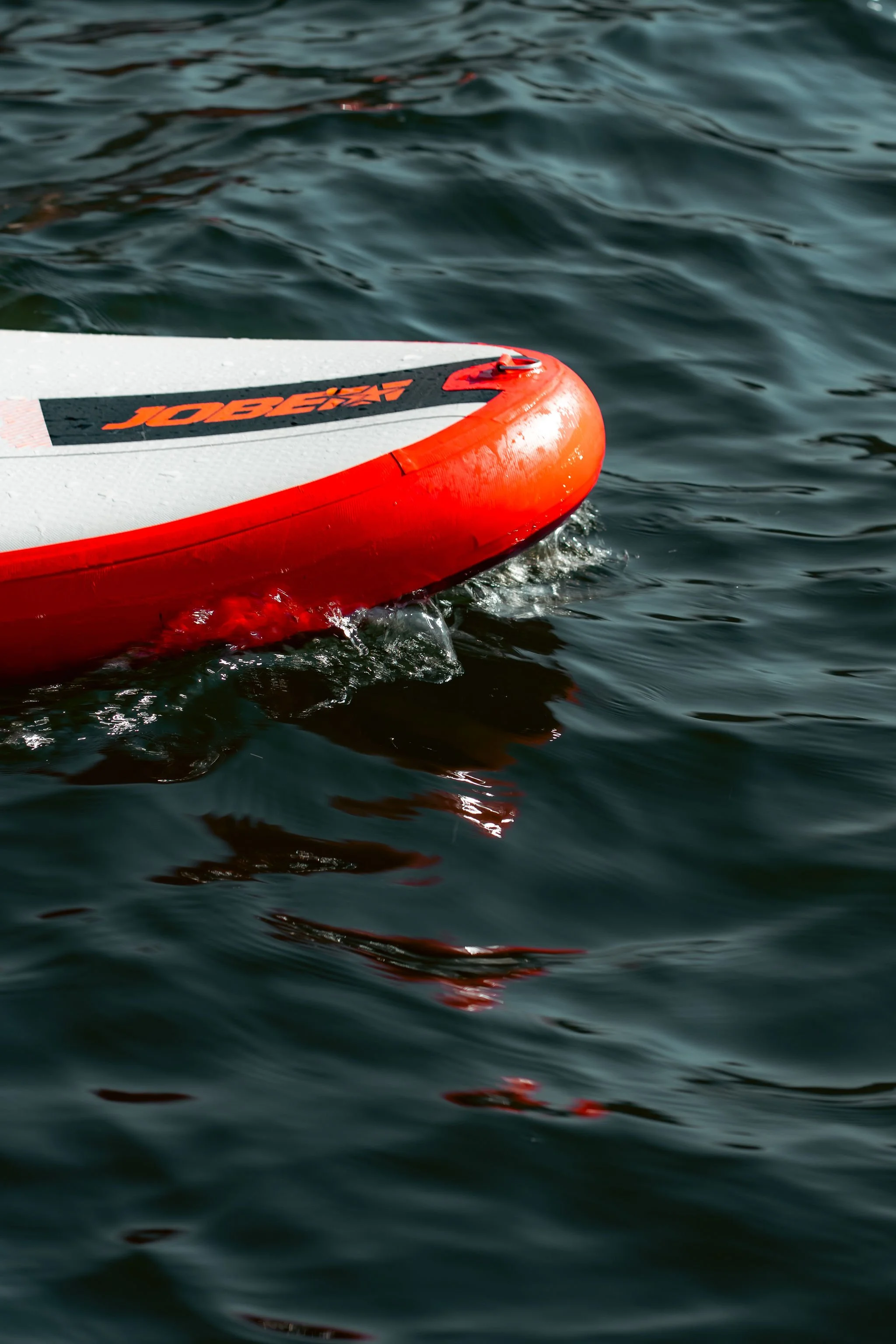 Close-up of a red and white stand-up paddleboard floating on dark water.
