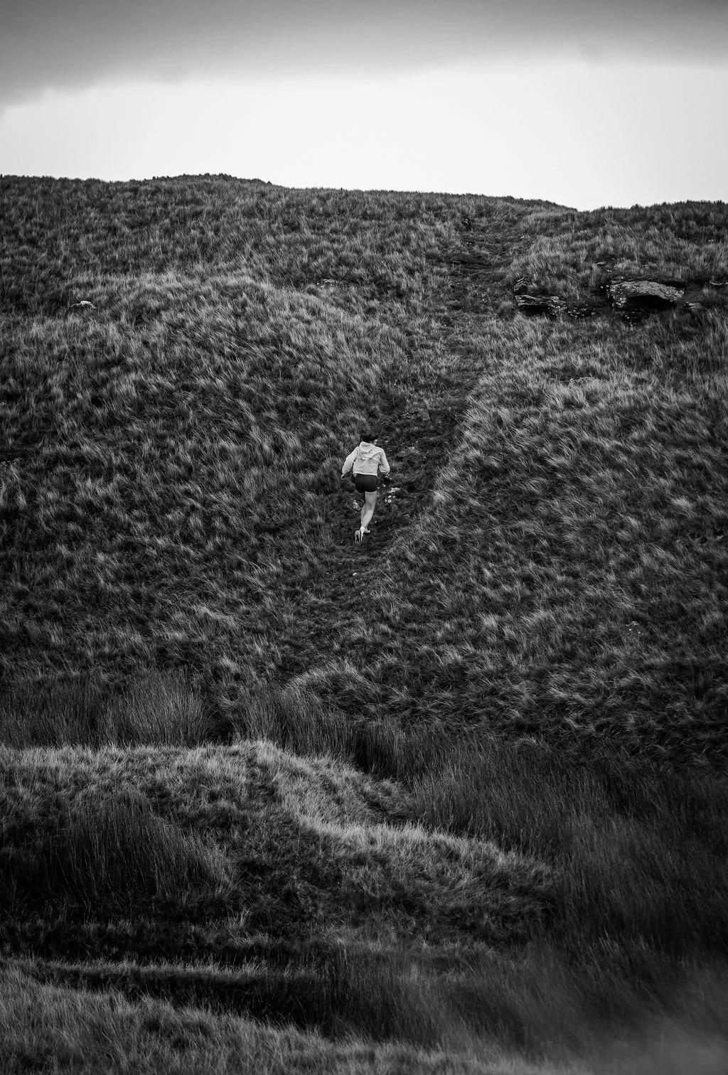 A person running up a grassy hill during overcast weather, captured in black and white.