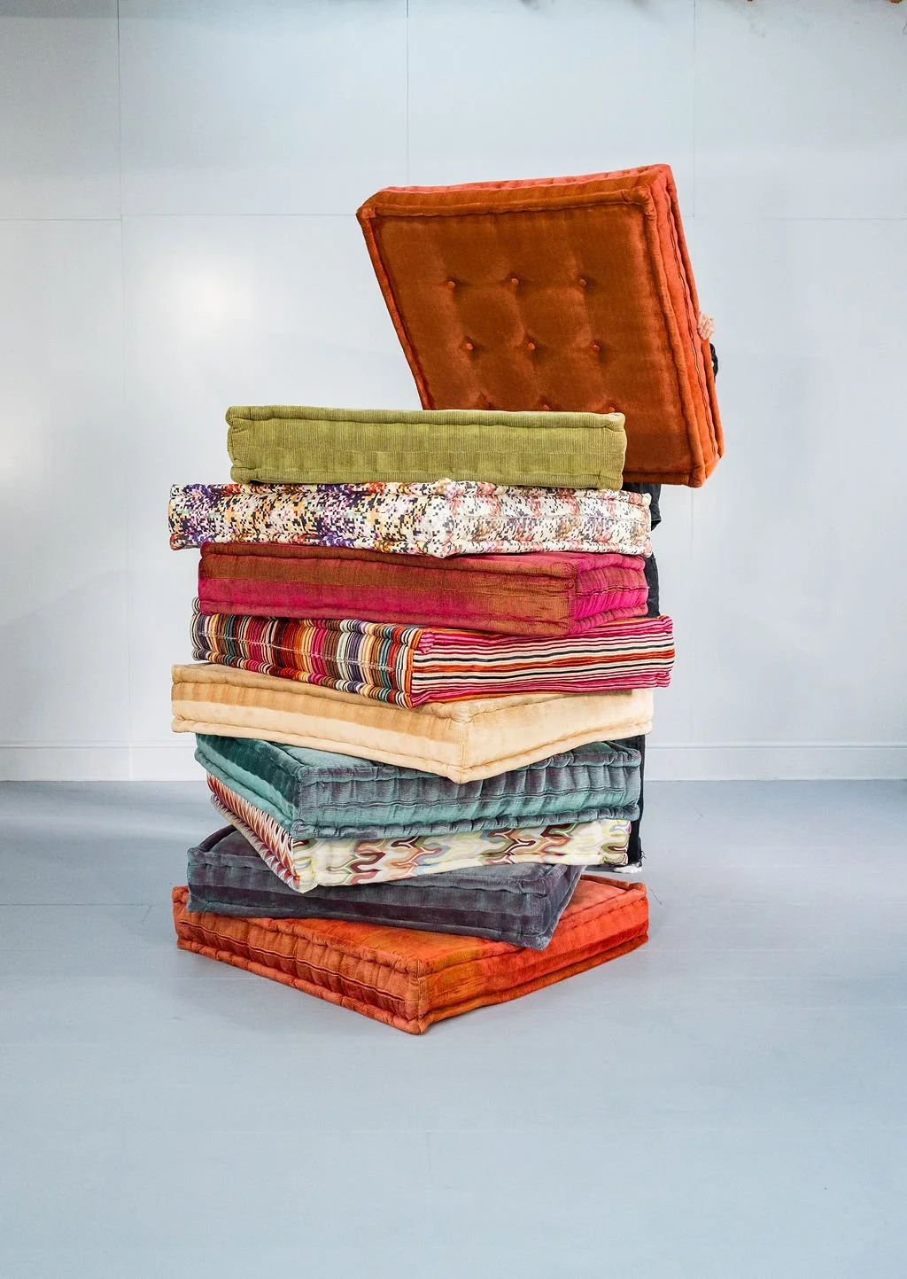 A stack of colorful vintage cushions and upholstered seats arranged on a corner of a white room.