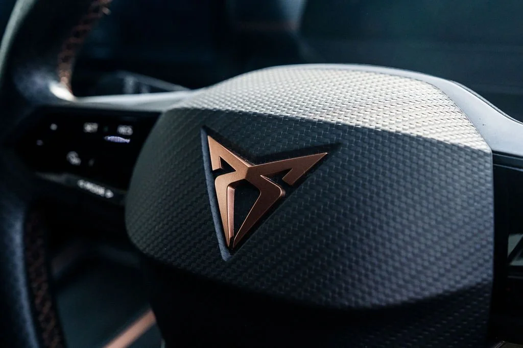 Close-up of a car steering wheel with a metallic logo in the center.