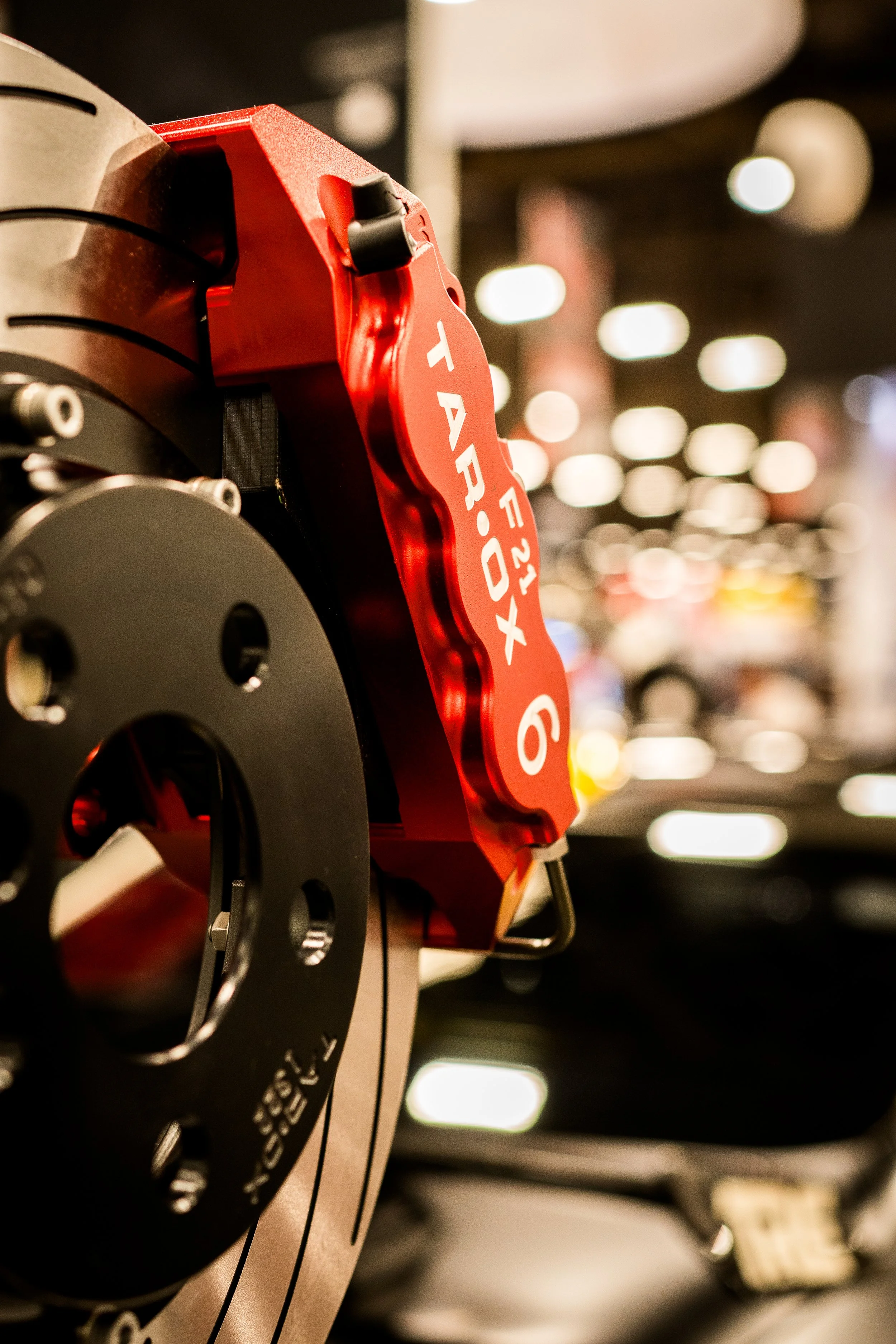 Close-up of a car brake disc and a red brake calliper with the label 'F22 XP 9 T ARTOX' in a showroom or display area.
