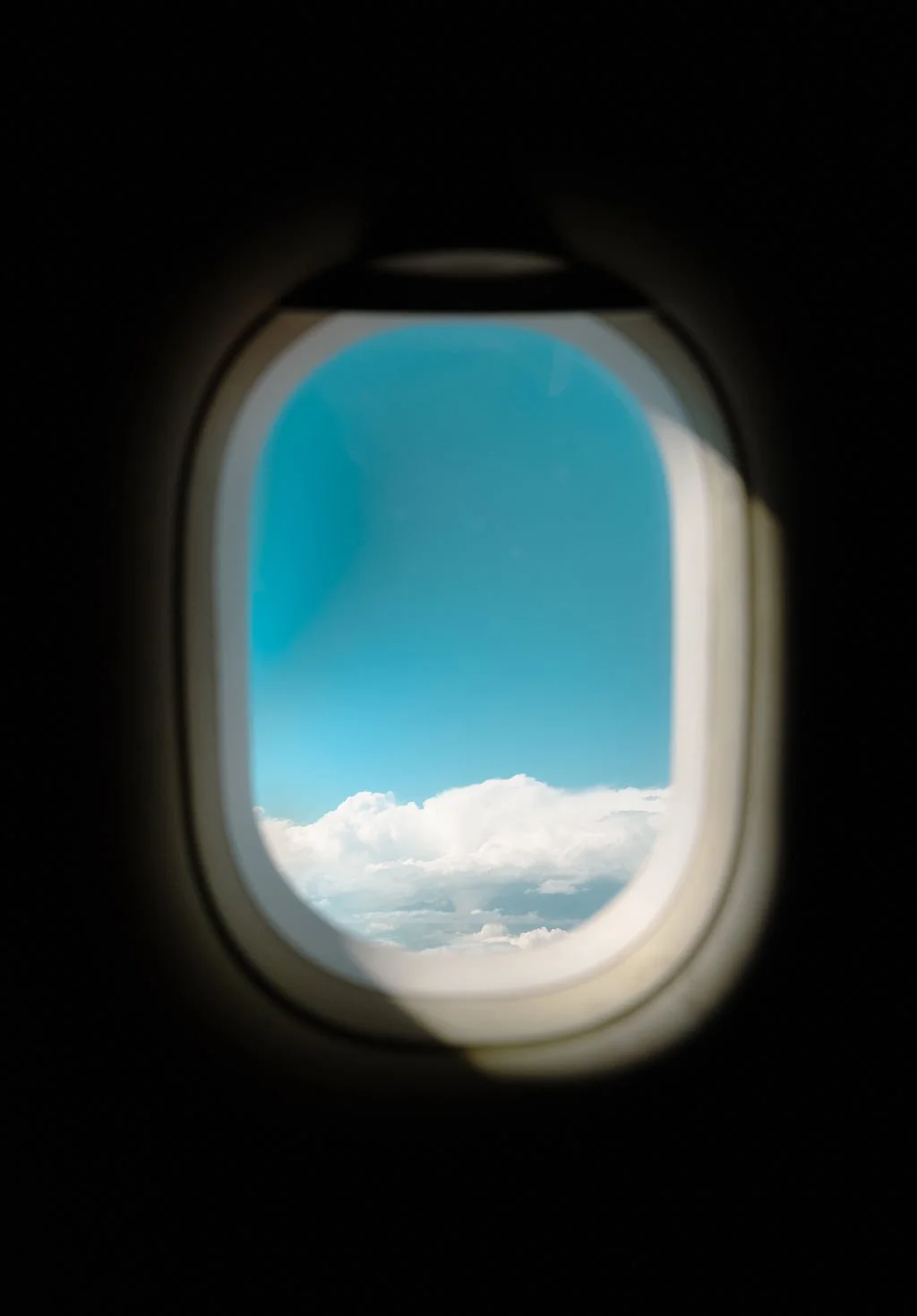 View of blue sky and white clouds seen through an airplane window.