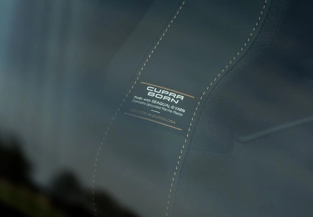 Close-up of a tag on a chair or fabric item, reading 'CUPRA BORN', made with SEAQUAL yarn, contains recycled marine plastic, created in Barcelona.
