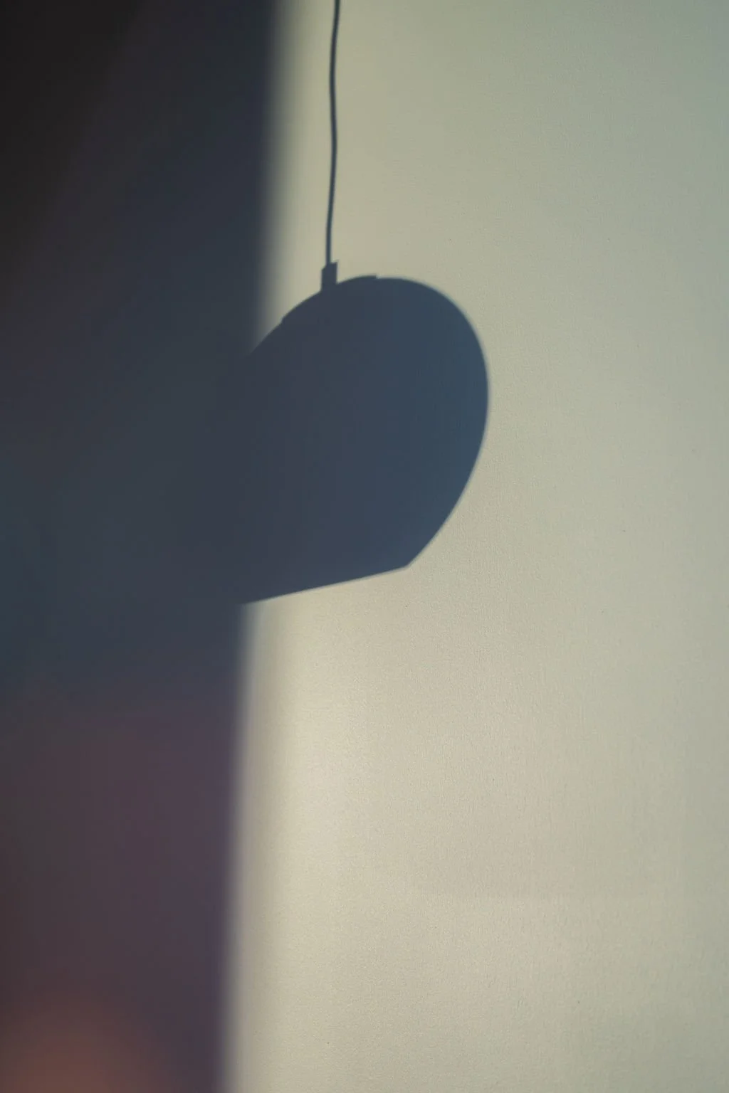 A shadow of a computer mouse cast on a wall, with the mouse hanging from a thin wire or cord.