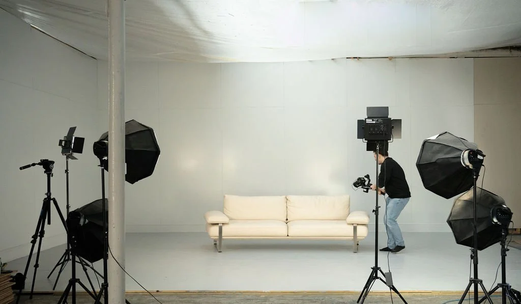 Photography studio setup with a white sofa, studio lights, and a photographer adjusting equipment.