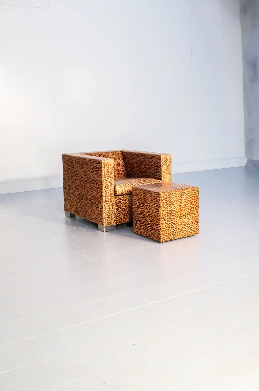 A single orange patterned armchair with matching ottoman on a light gray floor against a white wall.