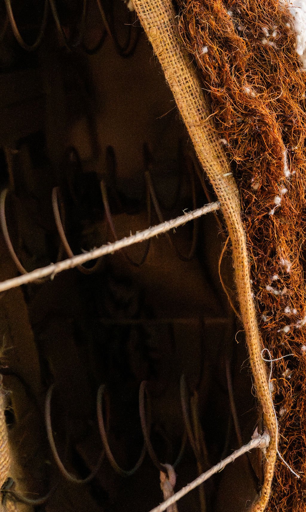 Close-up of a vintage stringed furniture, showing the interior with numerous metal pegs, and part of the outer casing with worn fabric and some brown fibers.