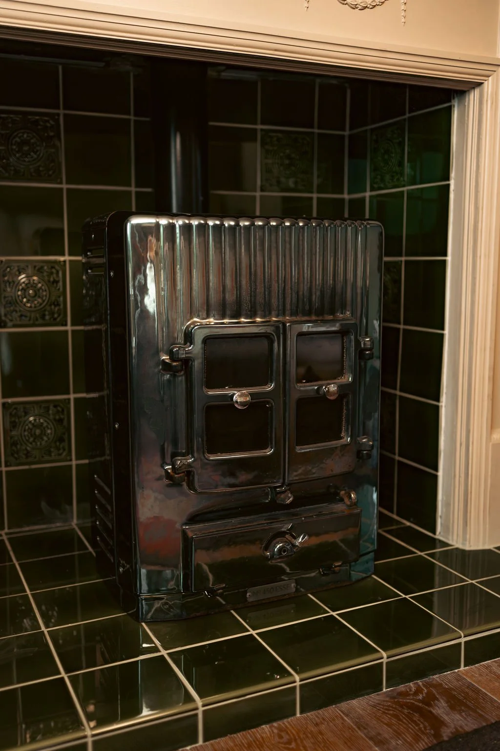 A vintage black and silver toy stove with four small stove windows, placed on a black tiled countertop and backsplash in a kitchen.