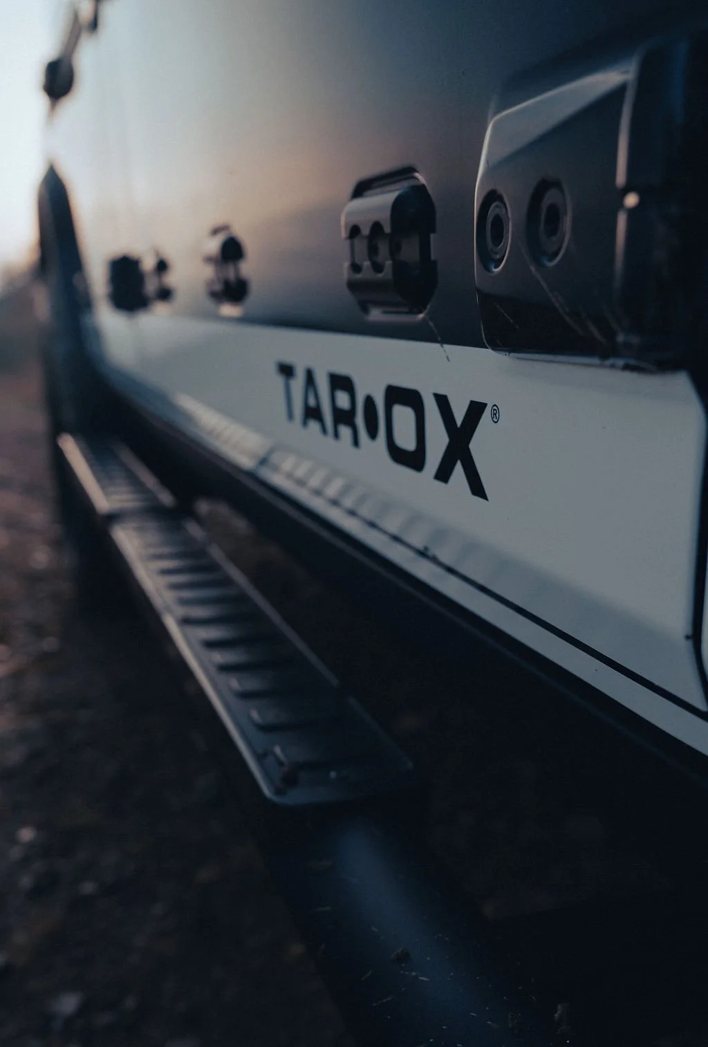 Close-up of a black vehicle with the branding 'TAROX' on the side, showing part of the step and side-mounted sensors or cameras.