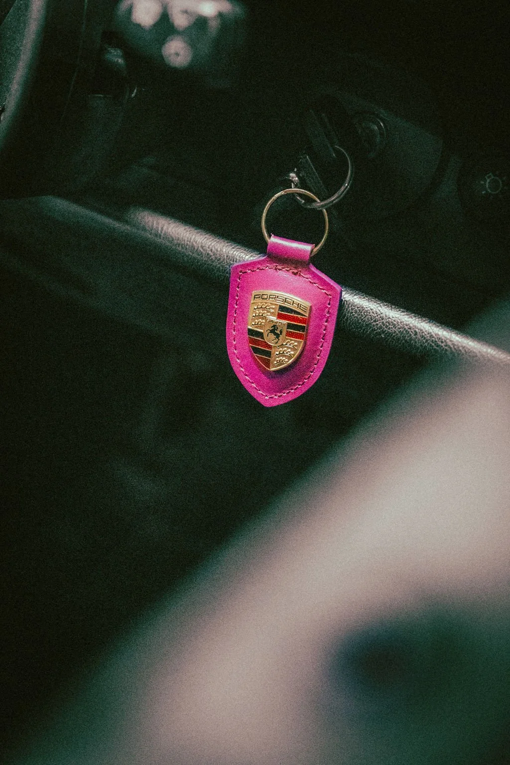 A Porsche keychain with a pink leather cover hanging from a car key in a vehicle.