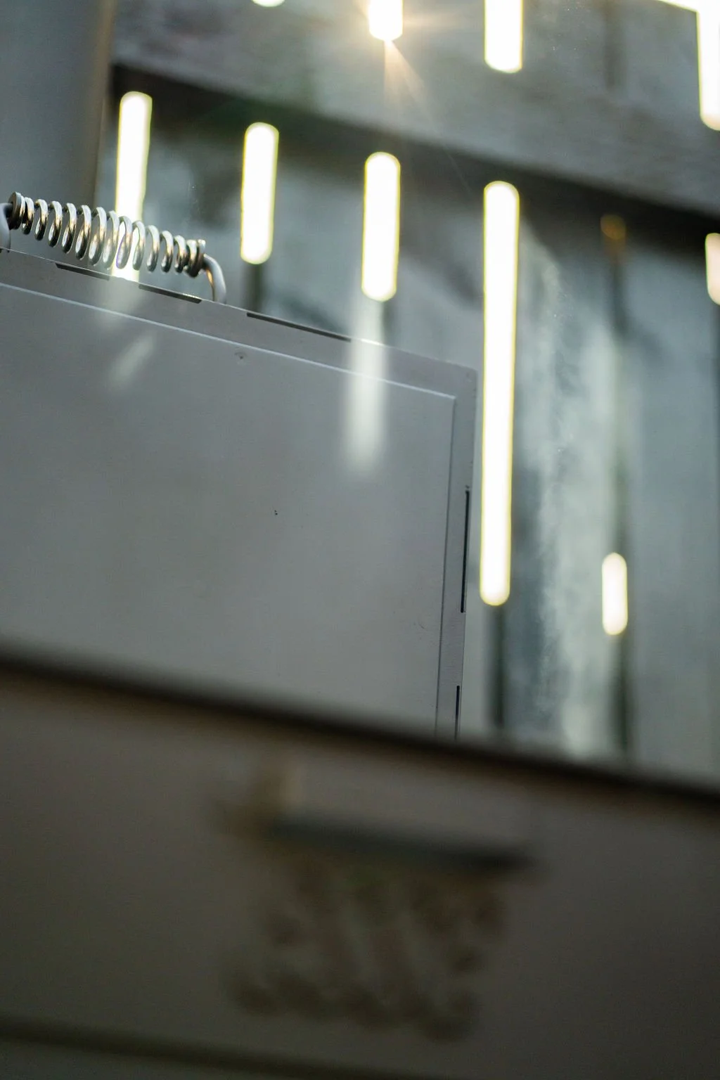 Close-up of a white cabinet with a top-mounted coil spring hinge, against a background of a wall with vertical light streaks and sunlight shining through, creating bright vertical lines.