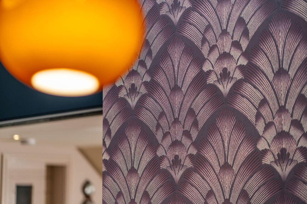 Close-up of a decorative wall with a purple and silver fan-shaped pattern. Part of an orange lampshade is visible in the foreground.