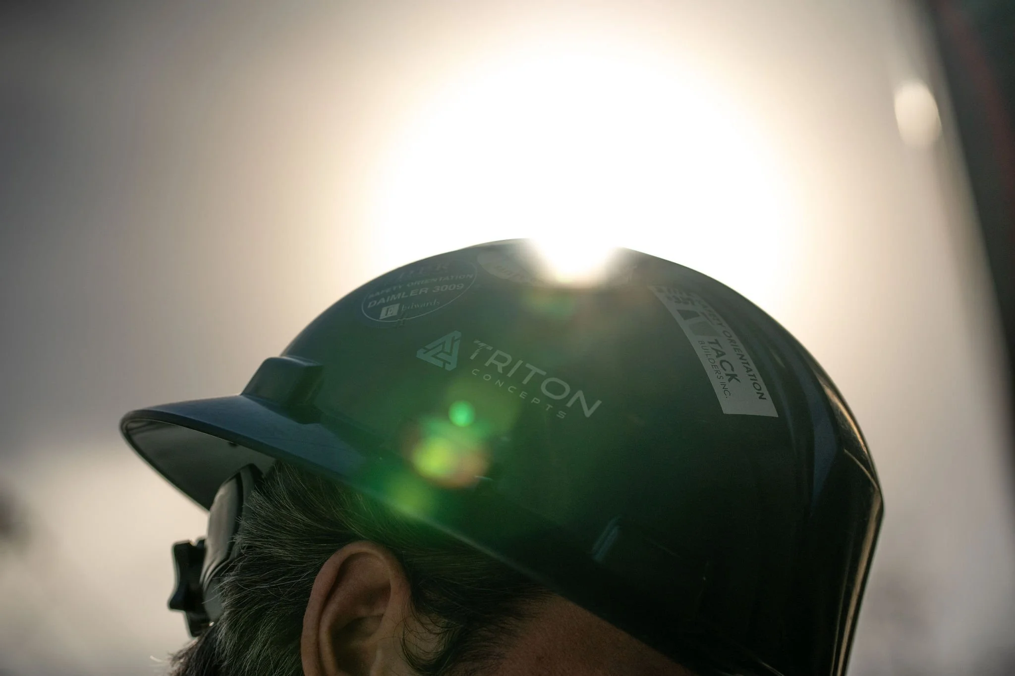 Close-up photo of a person wearing a black safety helmet with sunlight in the background.
