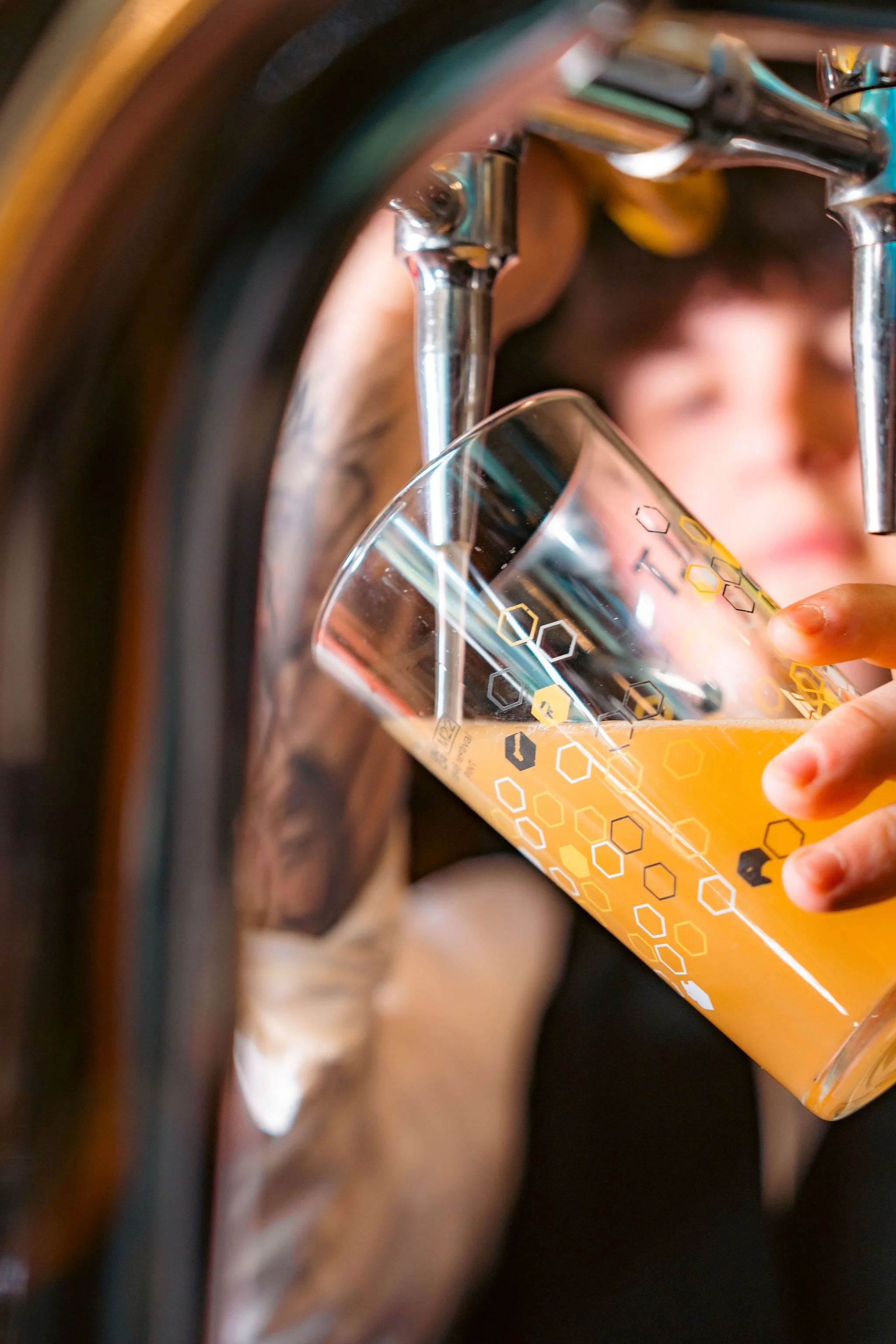 Person pouring craft beer from tap into a glass with a hexagon pattern design.