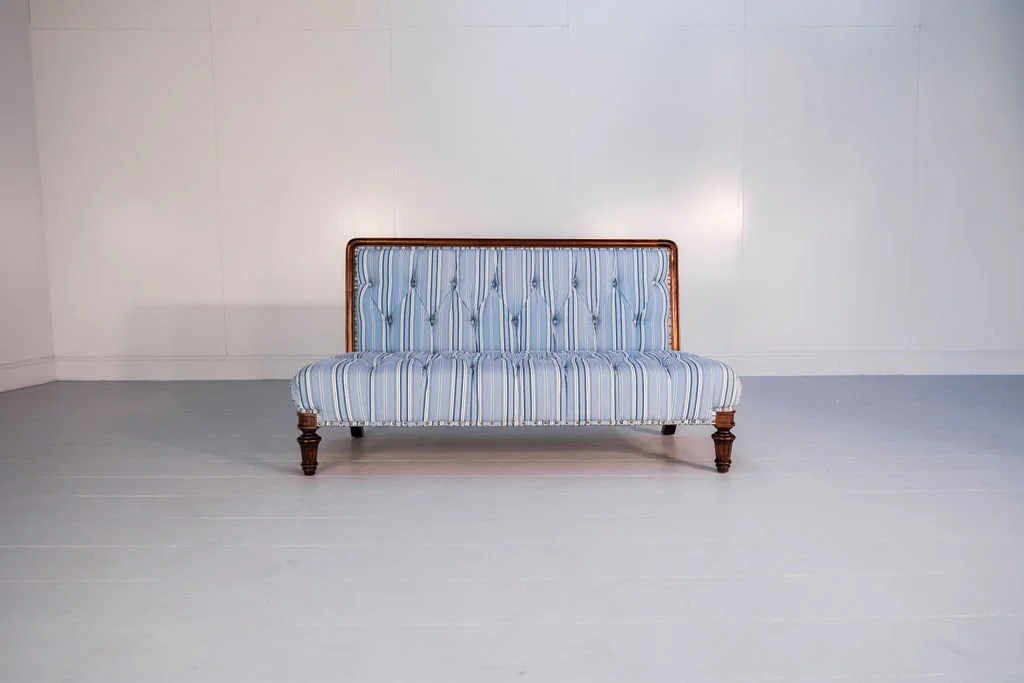 A vintage blue striped sofa with wooden legs and trim, placed against a plain white wall in a minimalistic room.