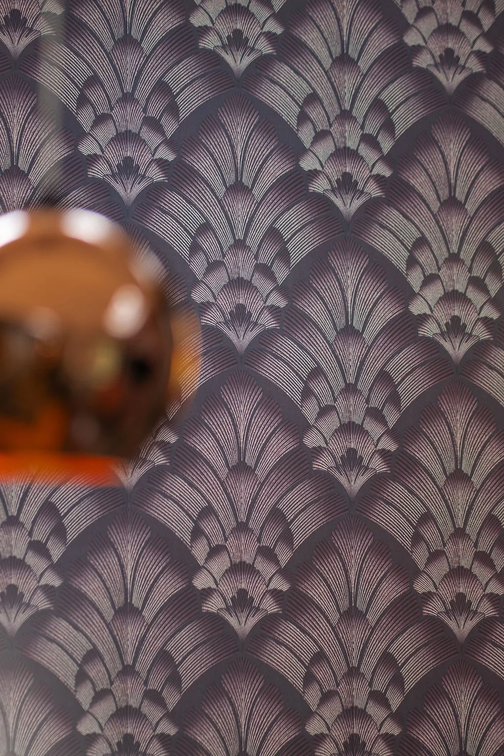 Close-up of a wallpaper with an intricate fan-like pattern in shades of purple and gold, with a blurred object in the foreground.