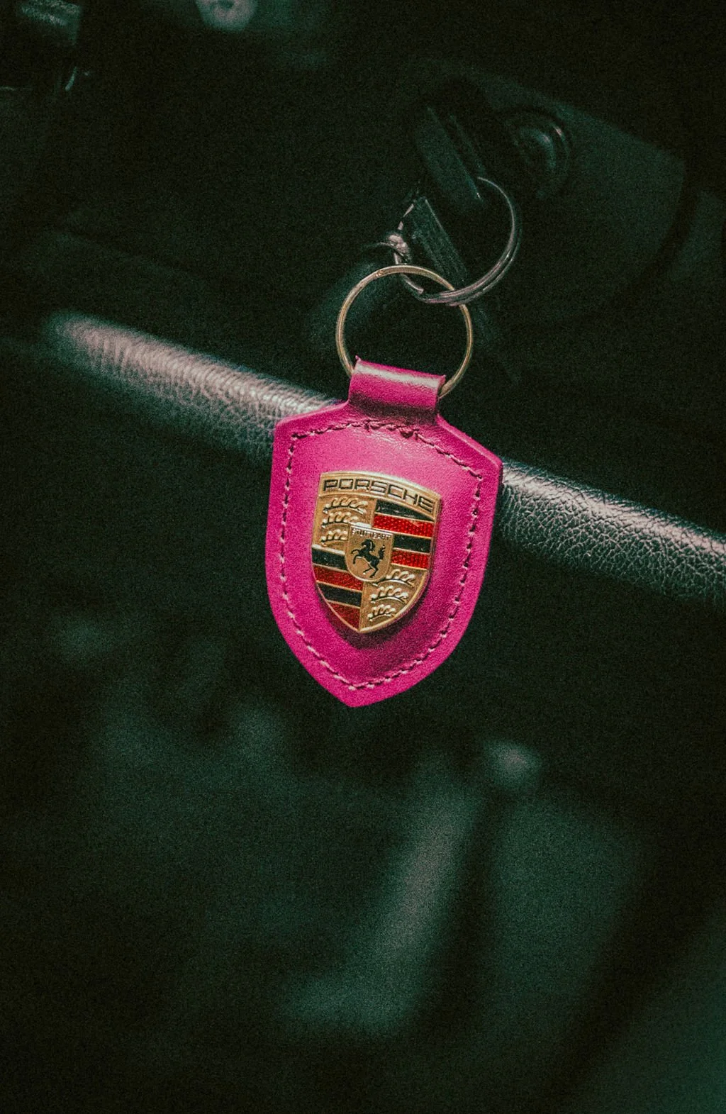 A pink Porsche keychain with a gold and black Porsche emblem attached to a set of keys inside a car.