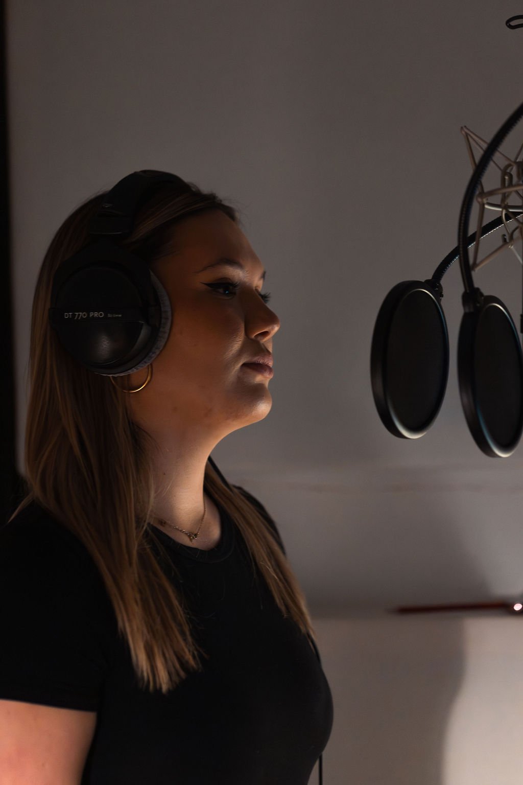 Woman recording vocals in a studio with headphones and a microphone.