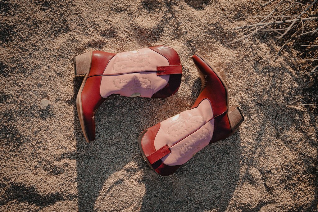 Red and white cowboy boots on sandy ground with some small twigs.