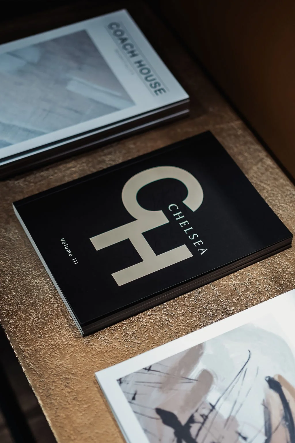 A booklet titled 'Chelsea" on a textured surface with other papers or magazines nearby.