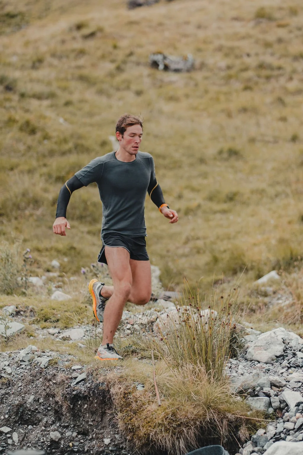 A young man running outdoors in a grassy, rocky landscape
