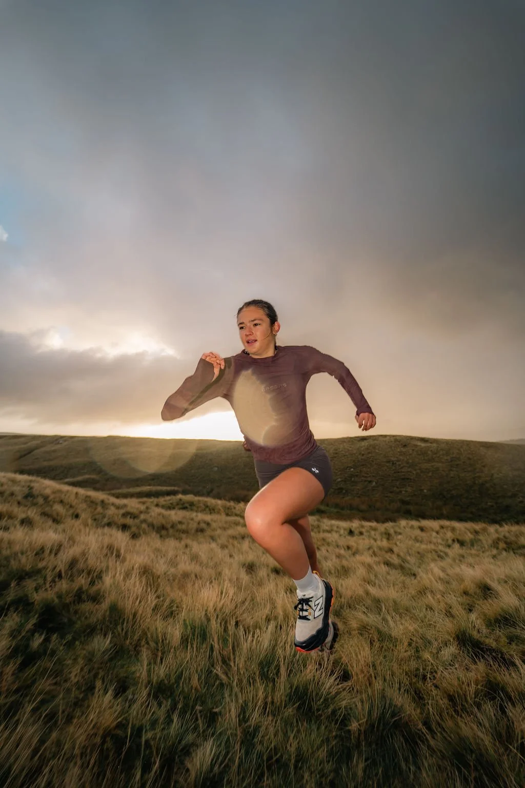 A woman running outdoors in a grassy field with hills in the background during sunset or sunrise.