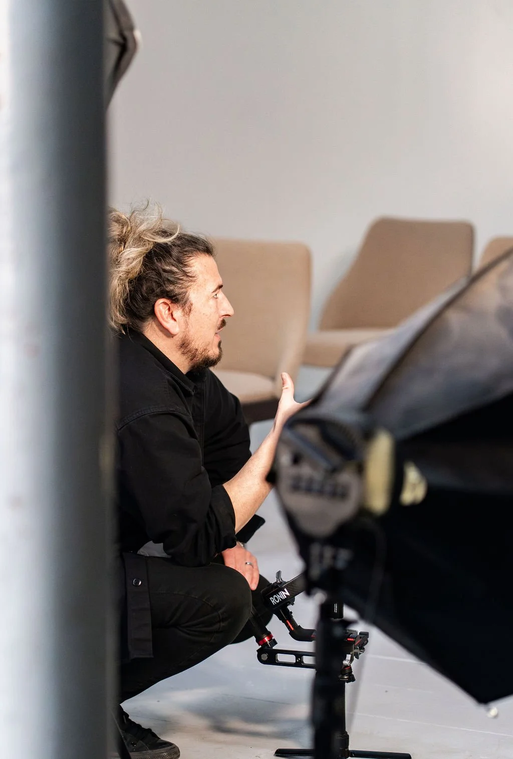 A man, wearing a black shirt, is kneeling and looking at a monitor while working on a film or video set.