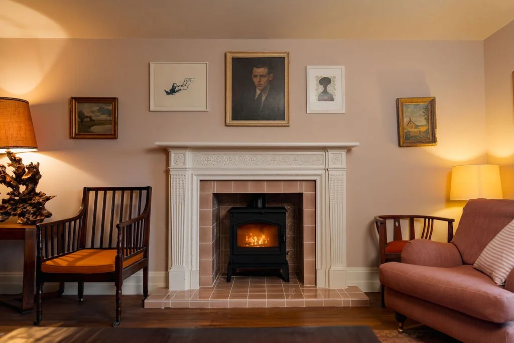 Living room with a fireplace, painting, and artwork on the wall, two armchairs and a pink sofa, and two lamps.
