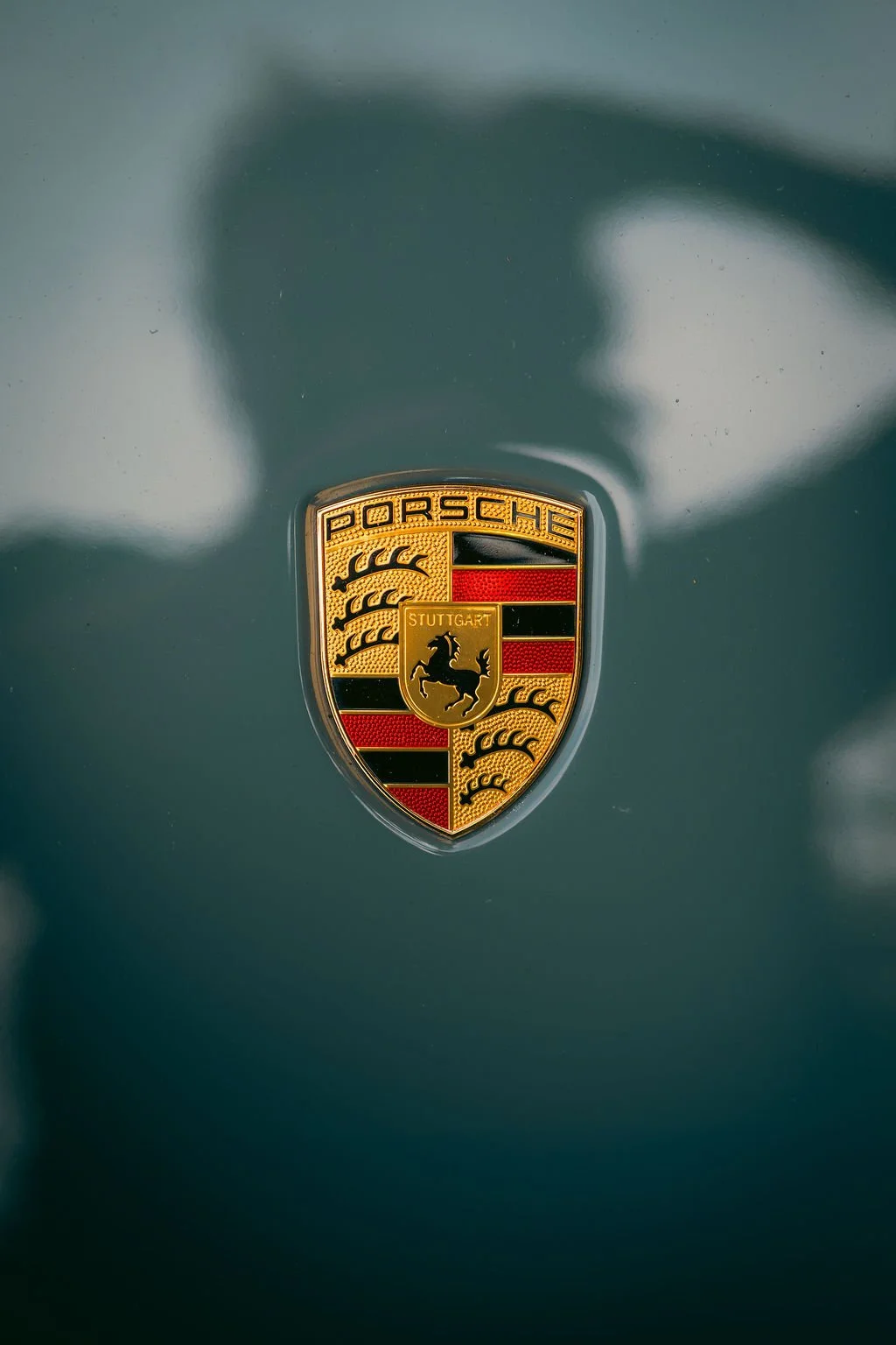 Close-up of a Porsche badge on a dark green car surface.