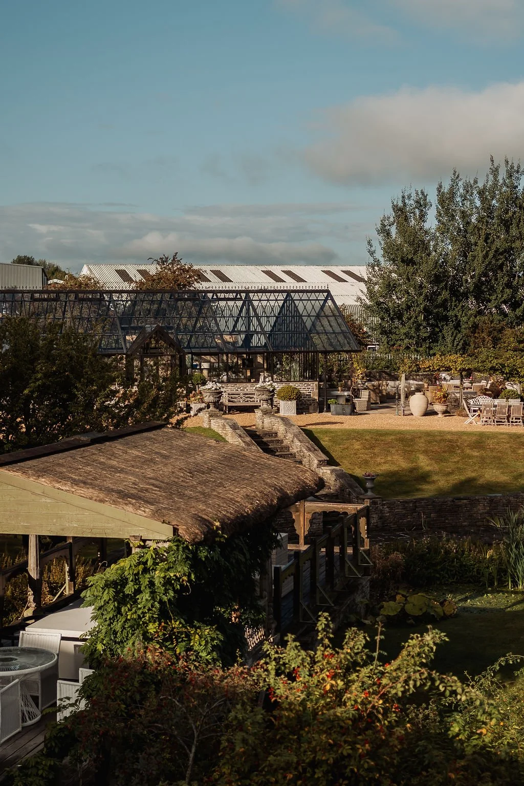 Exterior view of a garden with greenhouses, outdoor seating, trees, and sky.