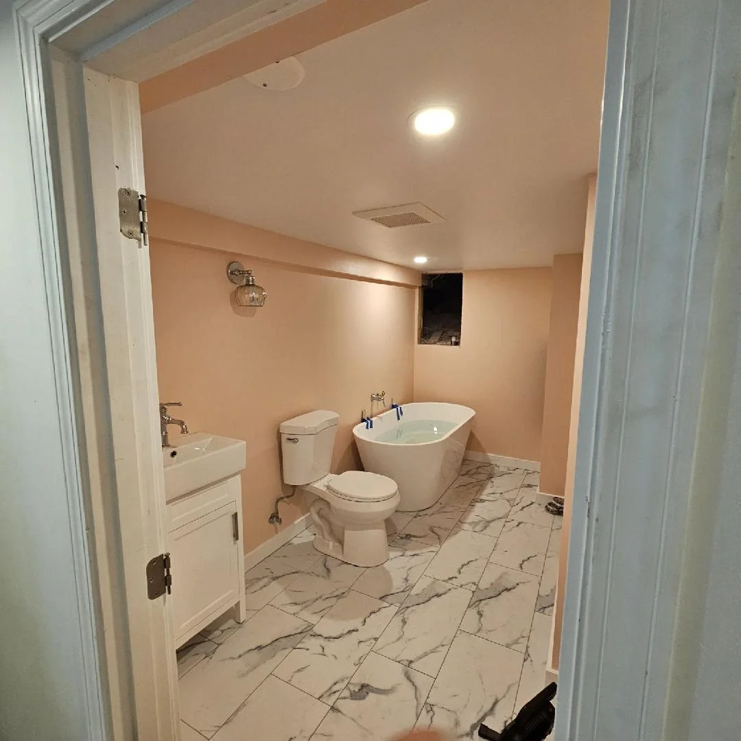 Bathroom remodel by Jepsen Construction featuring a freestanding bathtub, marble-look tile flooring, and white vanity