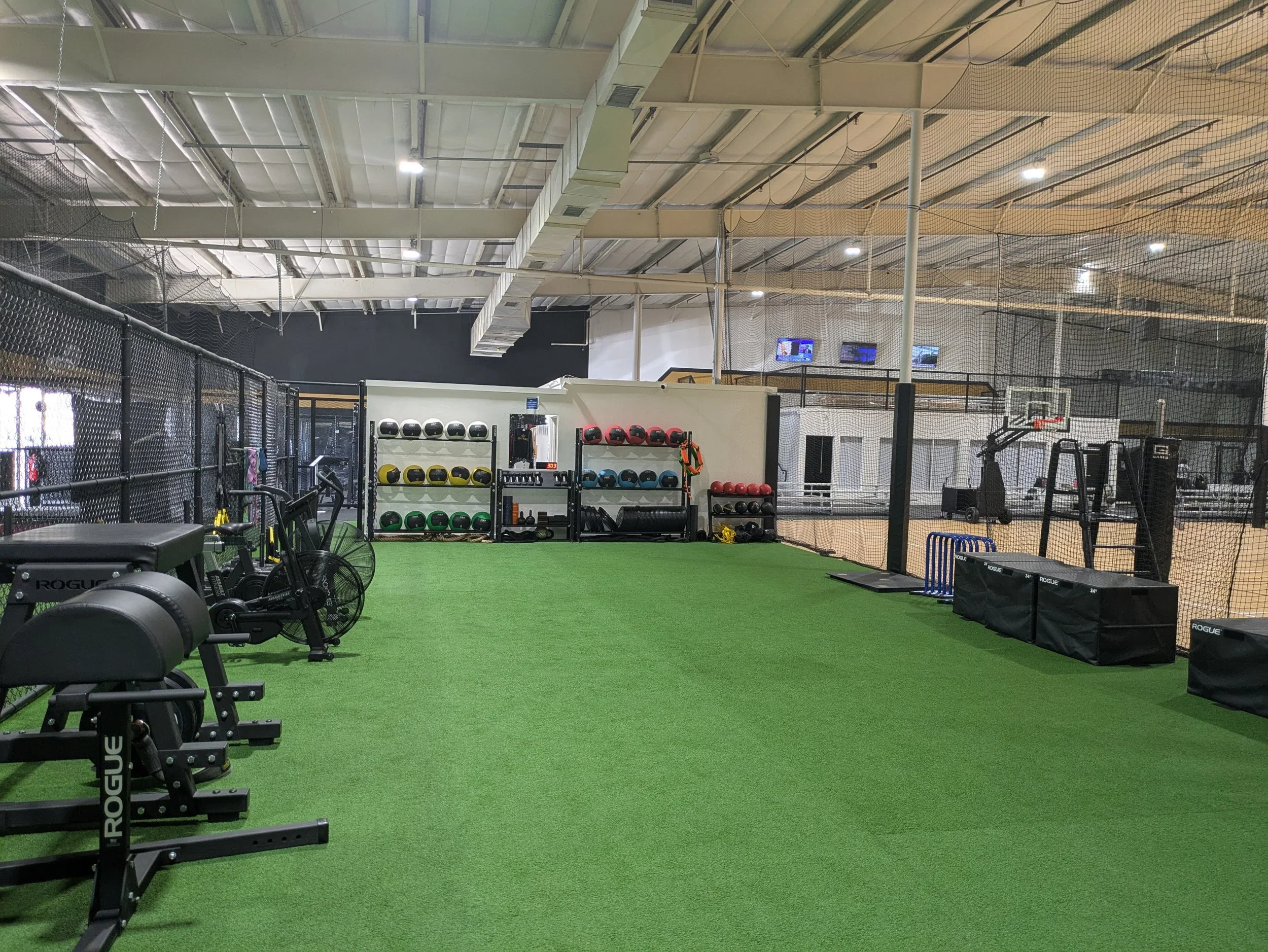 Indoor gym with green turf, fitness equipment, and a basketball court in the background.