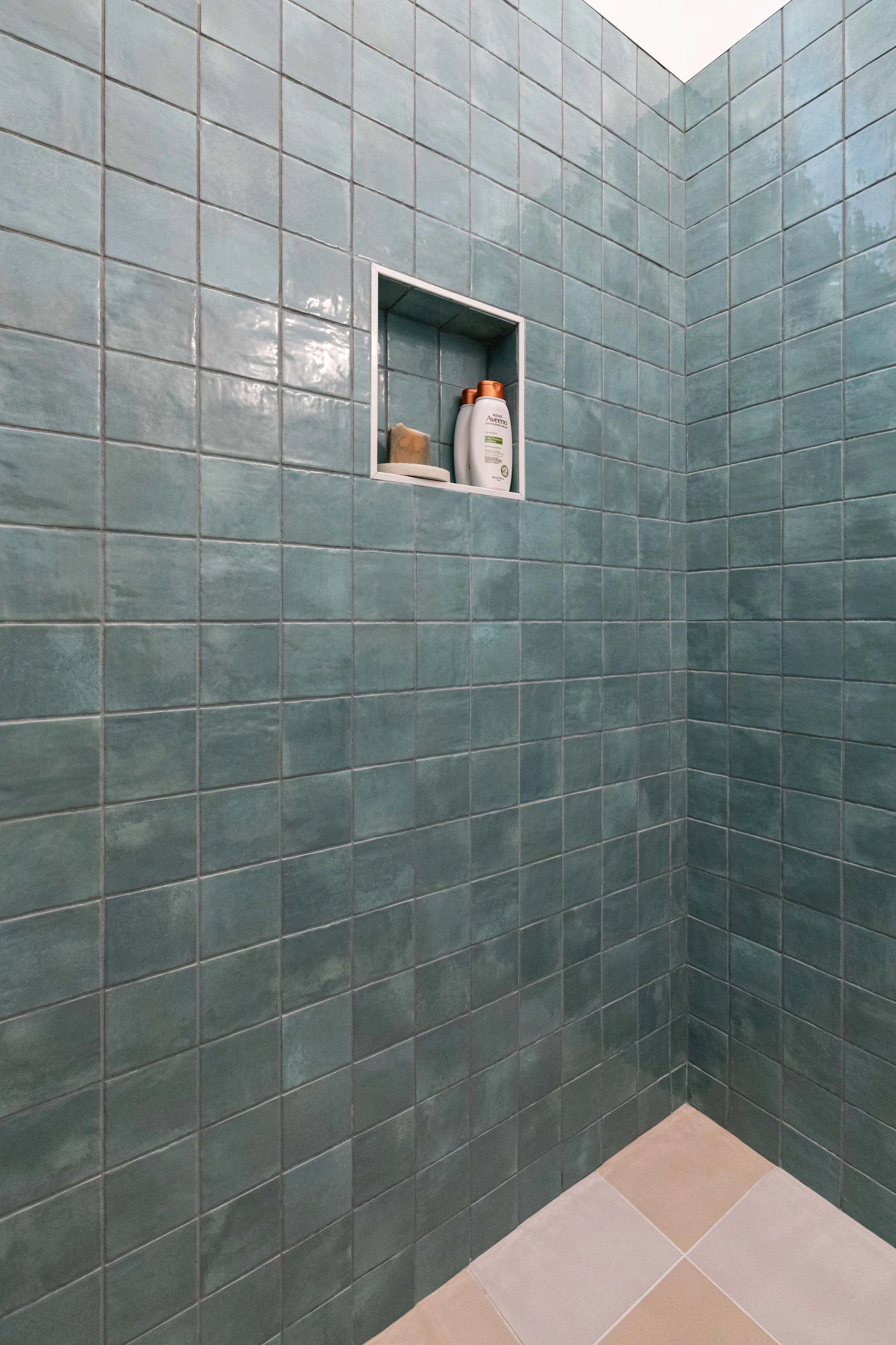 Green tiled shower wall with built-in niche holding shampoo, soap, and a small dish.