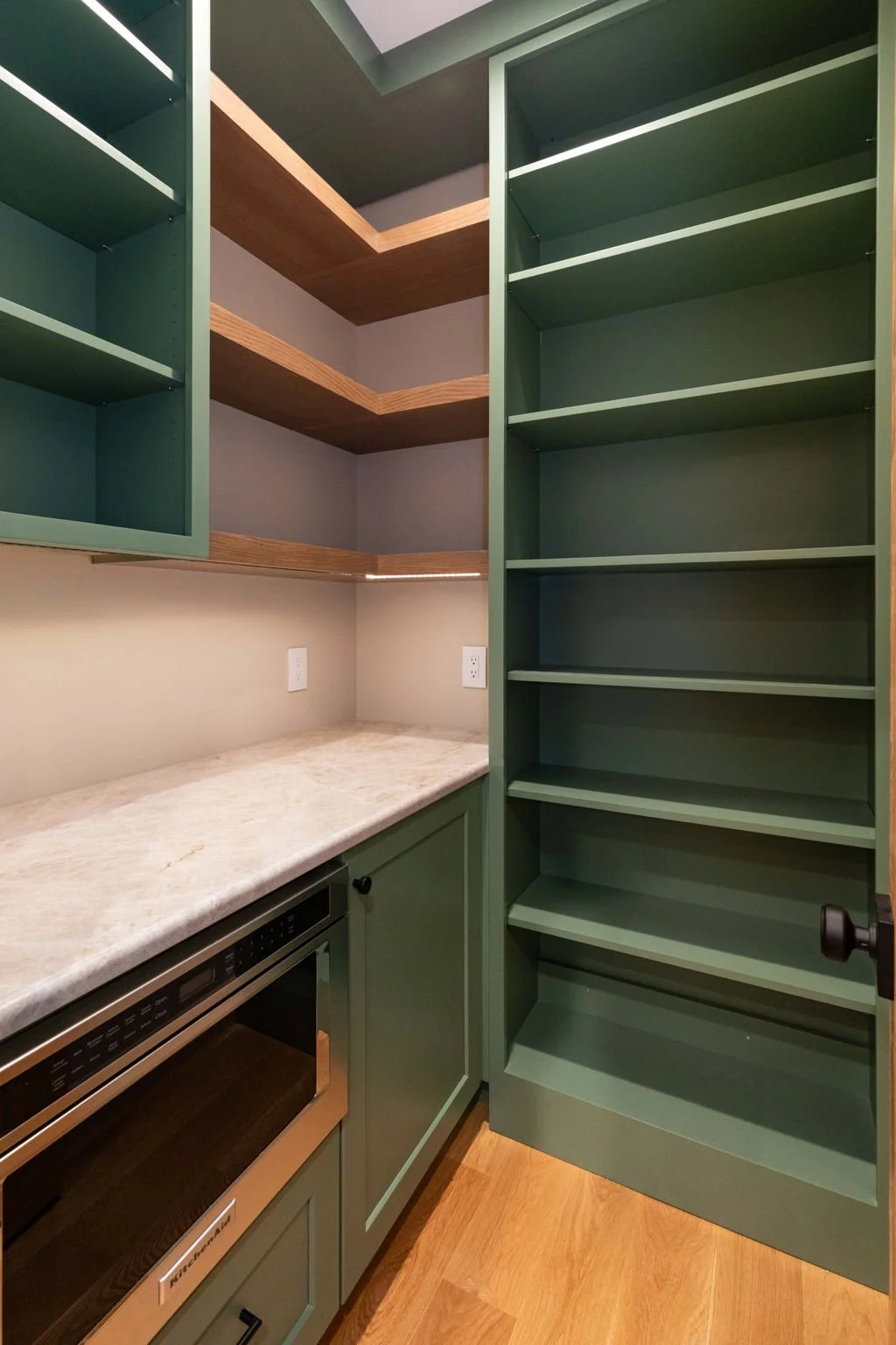 A kitchen cabinet and open shelving with a marble countertop. The cabinet is painted green, and the shelves are empty. There are two electrical outlets on the wall behind the countertop.