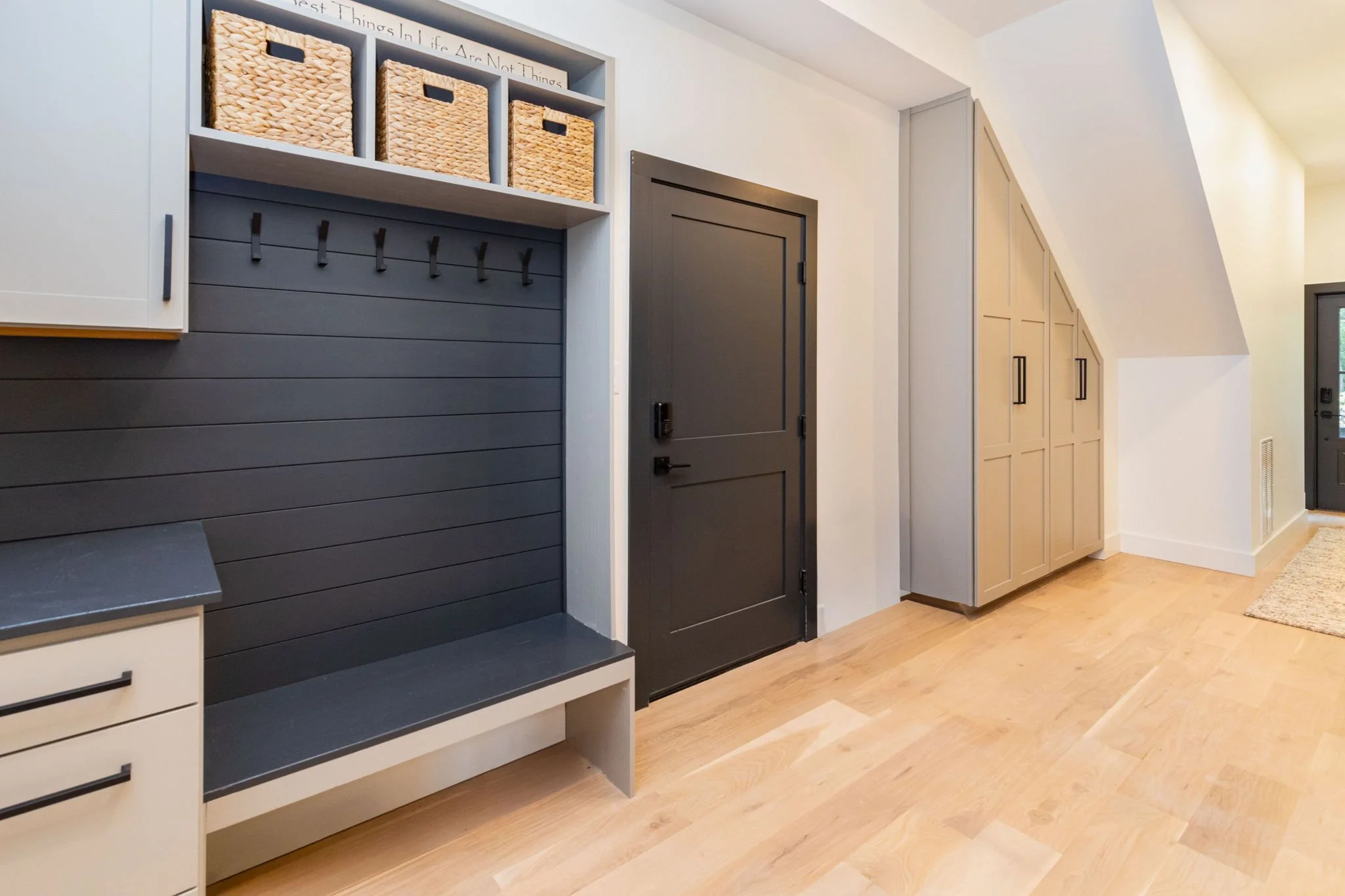 Entryway with black door, beige cabinetry, black hooks, and woven baskets