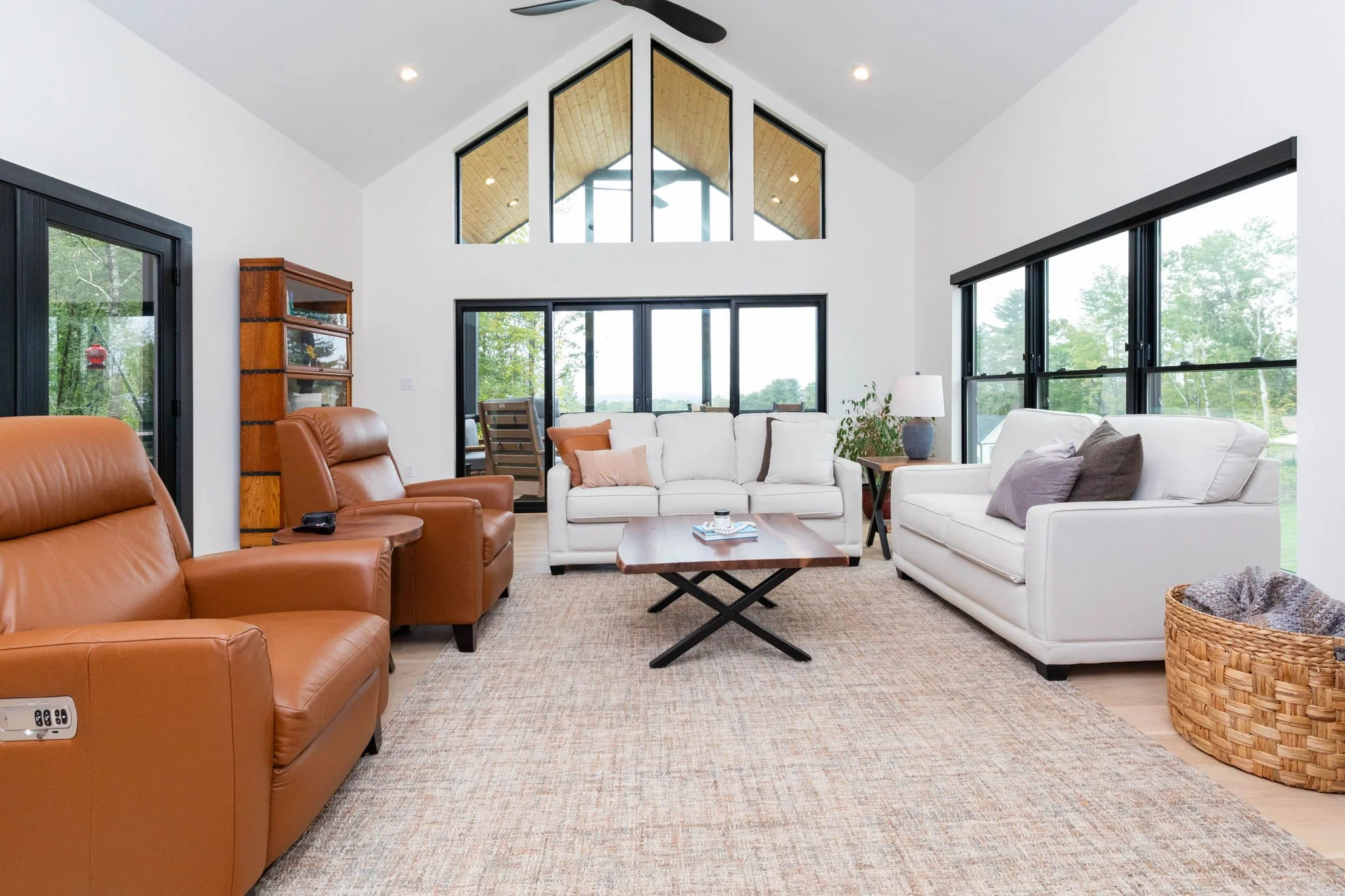 Living room with white and brown sofas, a wooden coffee table, and large windows showing outdoor greenery.