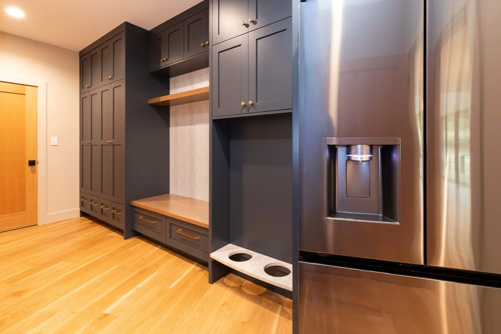 Modern kitchen with navy blue cabinets, wooden doors, and stainless steel refrigerator with water and ice dispenser, hardwood floors, and a countertop with open shelves.