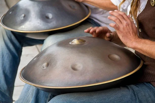 Menschen spielen auf Handpan- oder Hang-Instrumenten.