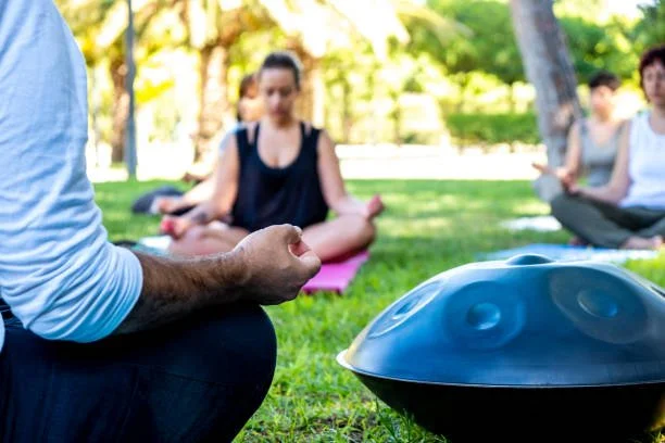 Menschen, die im Park an einer Yoga- oder Meditationssitzung teilnehmen, mit einem Handpan in der Nähe.
