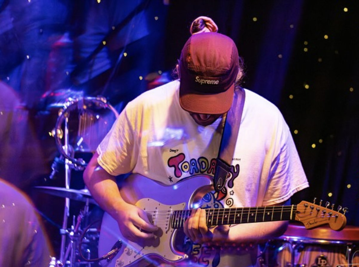 Man in red cap and white t-shirt is leaned over playing a guitar