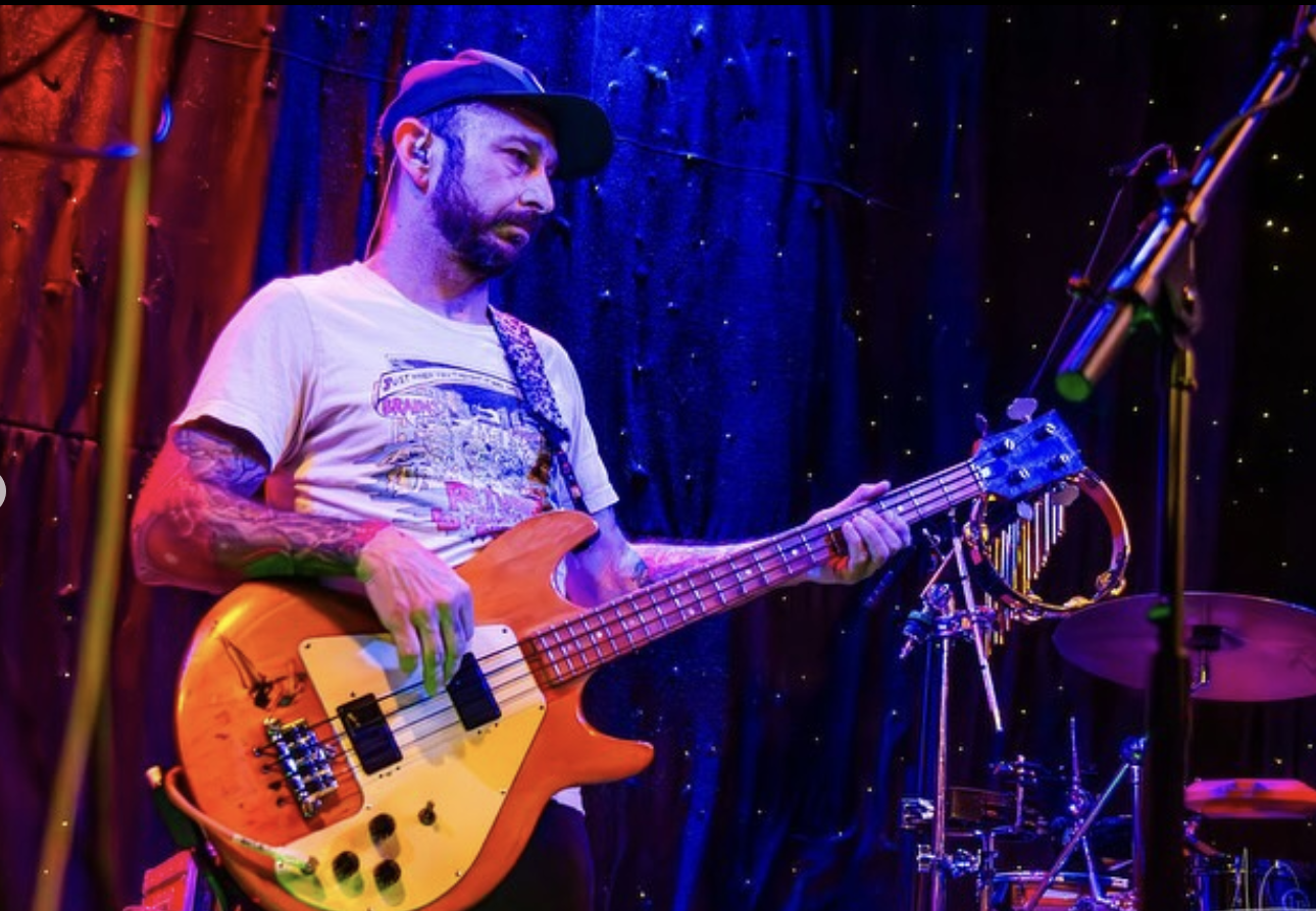 Man in black cap and white t-shirt is holding and playing a bass guitar