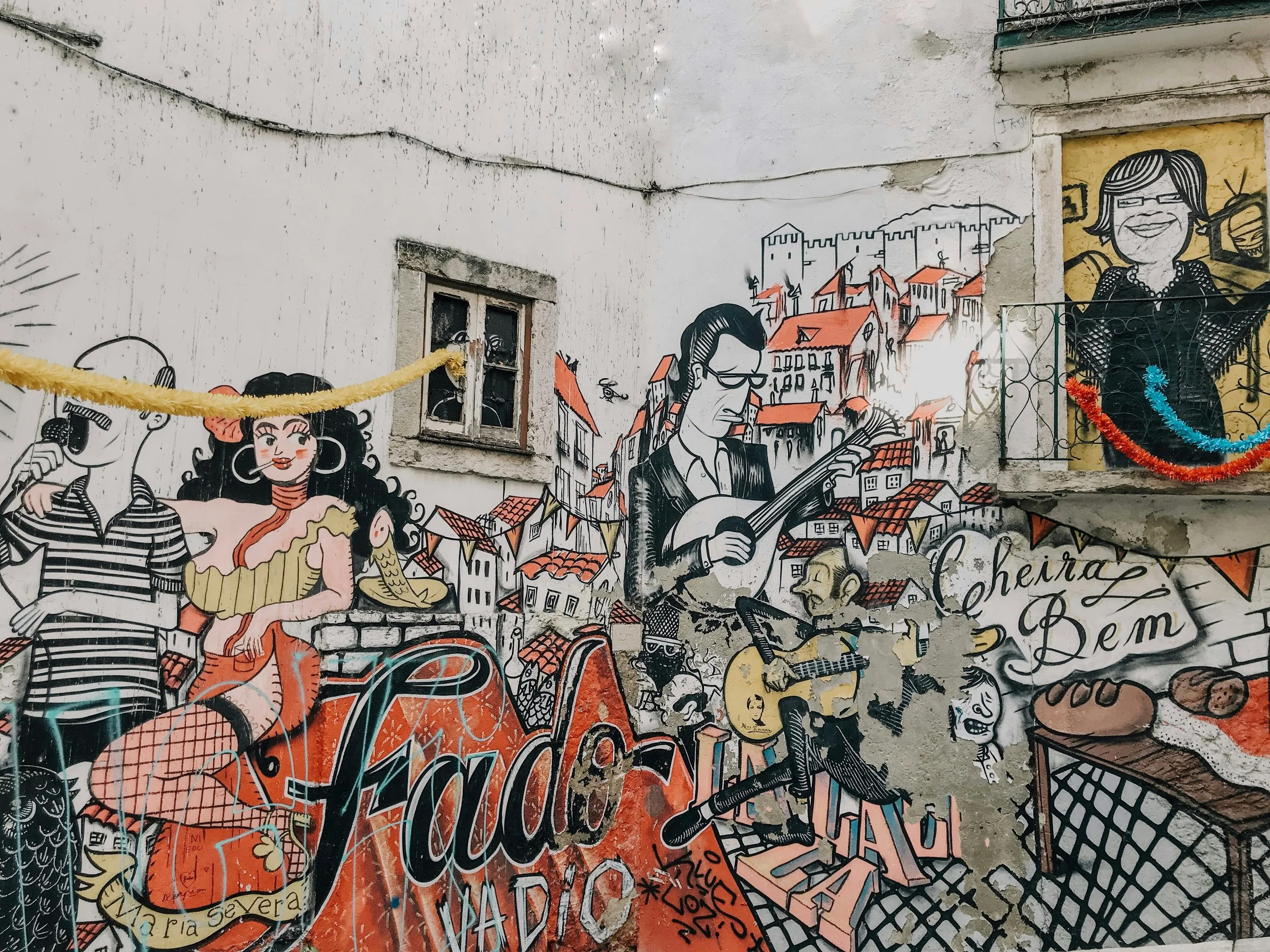 Colorful mural on a wall depicting people, buildings, and musical instruments with a restaurant table with food in the corner.