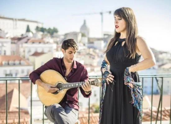 Fado singer with traditional shawl accompanied by male musician playing traditional Portuguese guitar. Overlooking Lisbon.