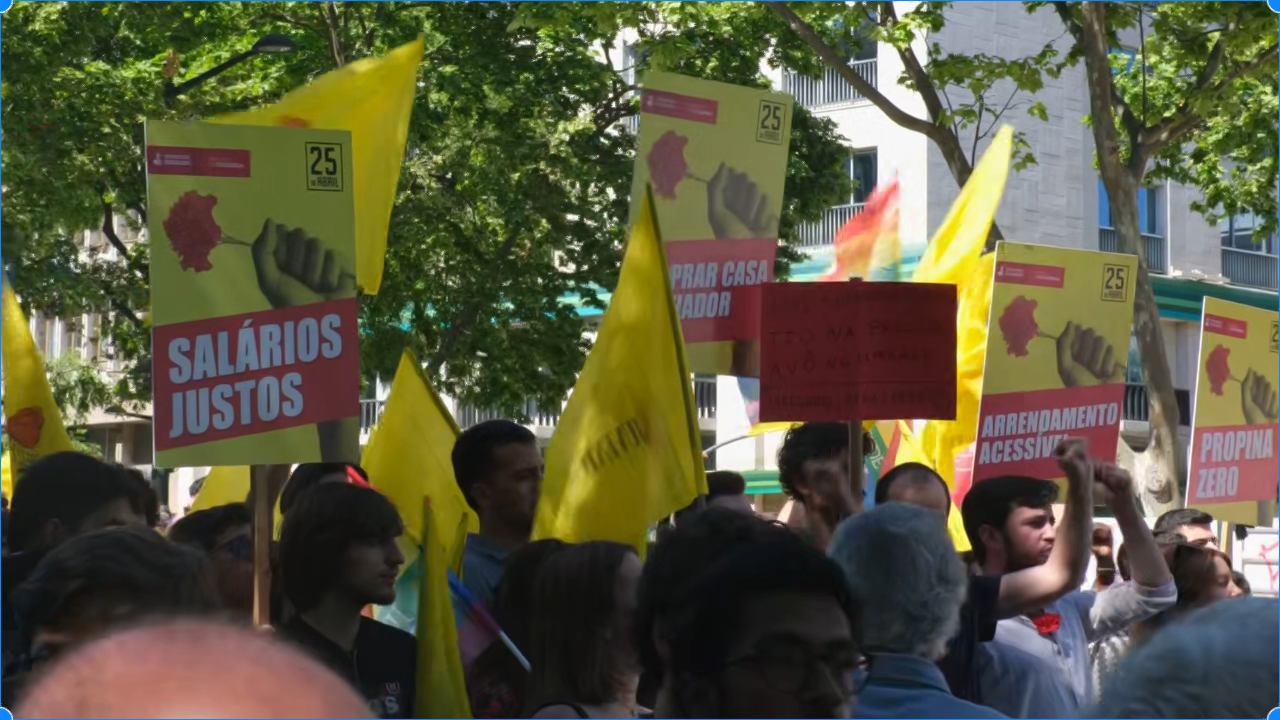 People marching in Portugal to celebrate April 25, o Dia da Liberdade, and May 1, o Dia do Trabalhador. Holding yellow and red signs and red carnations.