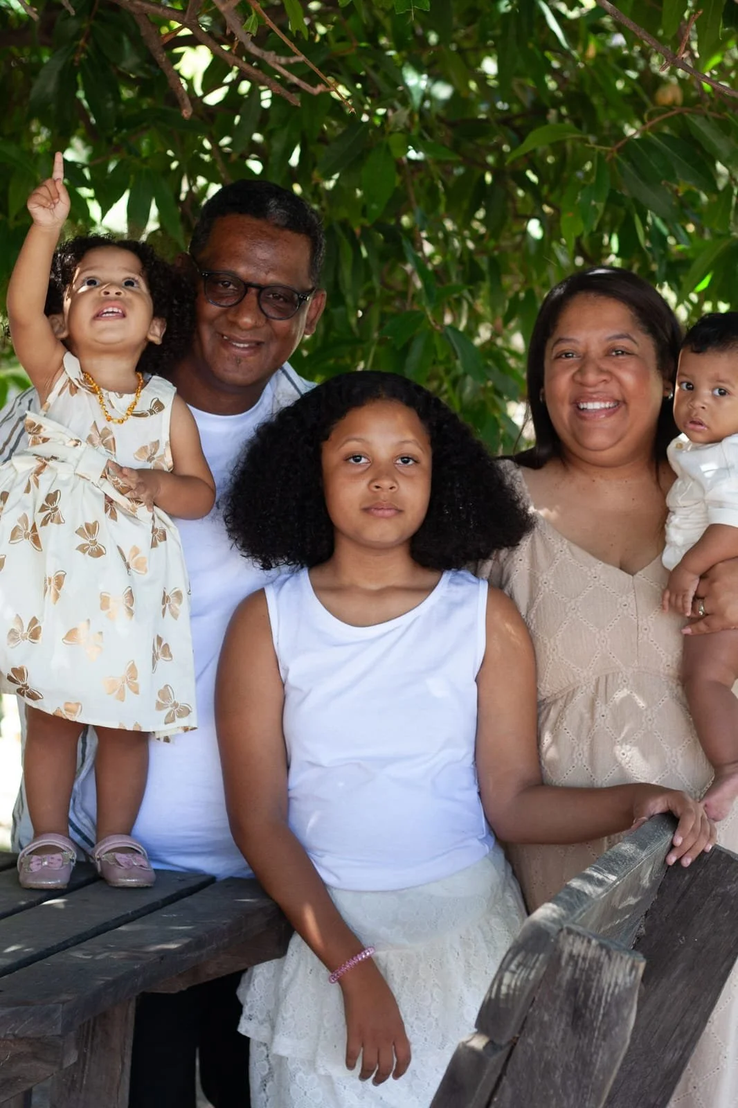 A family standing together, smiling, against a background of green tree branches.