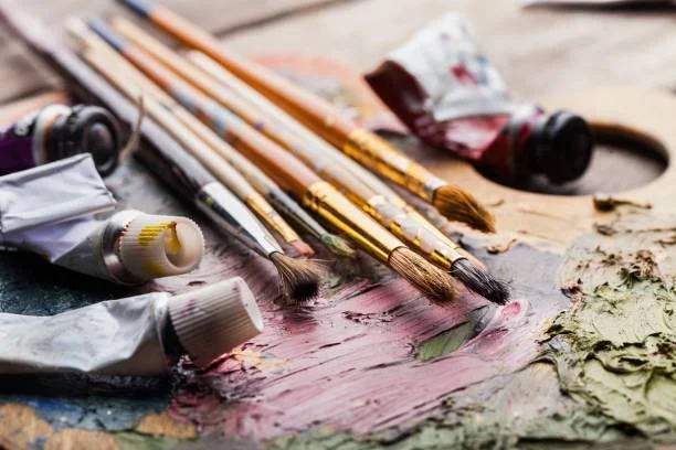 Paintbrushes and tubes of paint on a painter's palette with mixed colors.