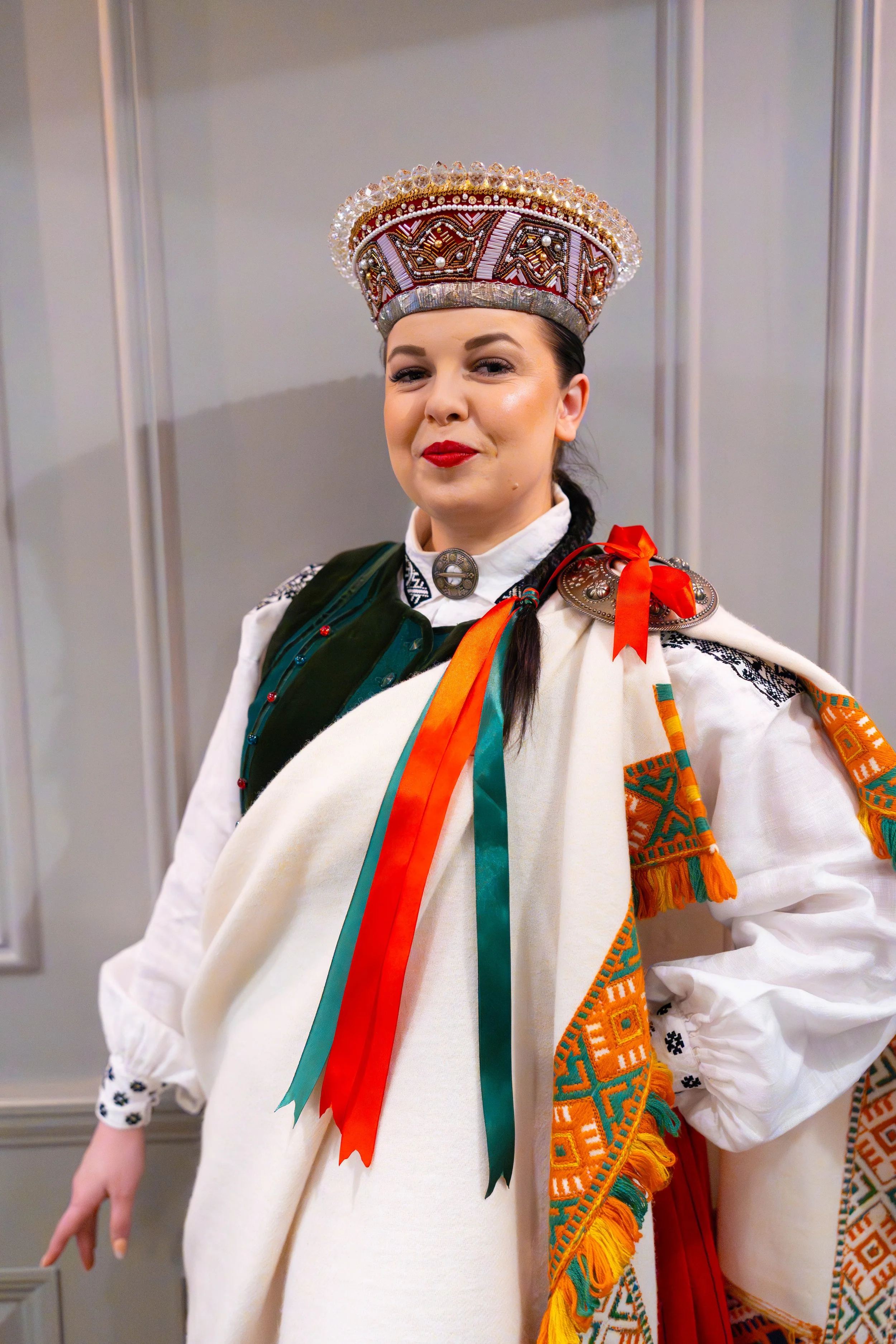 Woman in traditional Eastern European folk costume, wearing an ornate embroidered headdress with beads and crystals, and colorful ribbons and embroidered fabric on her clothing.